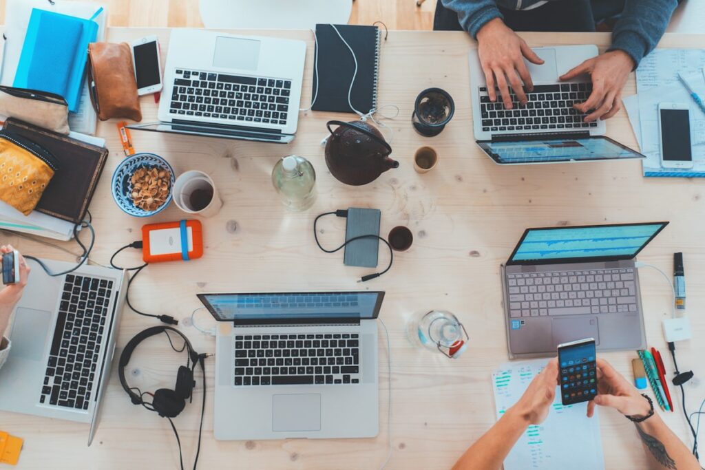 Mai multe persoane lucrand la laptopuri, una langa alta
