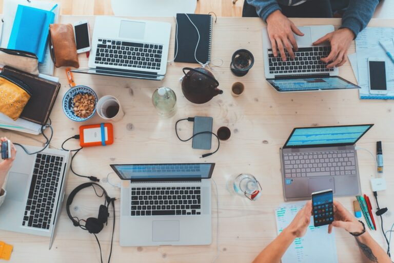 Mai multe persoane lucrand la laptopuri, una langa alta