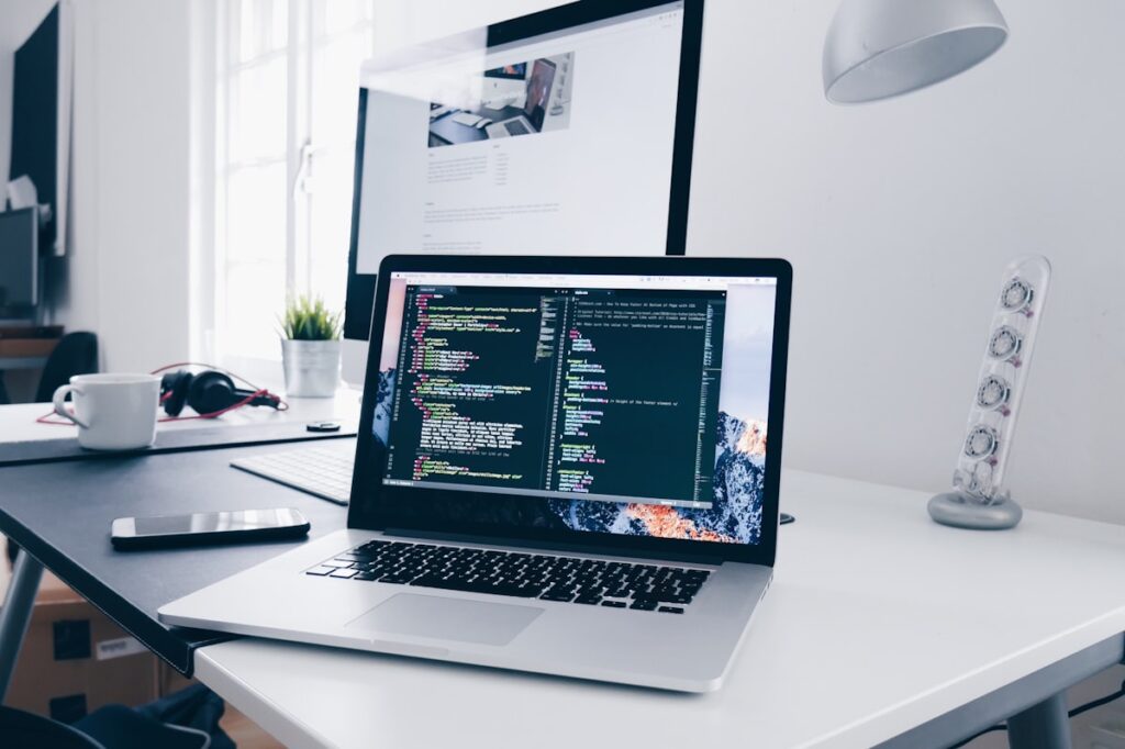 Laptop deschis pe birou, cu un editor de cod pe ecran